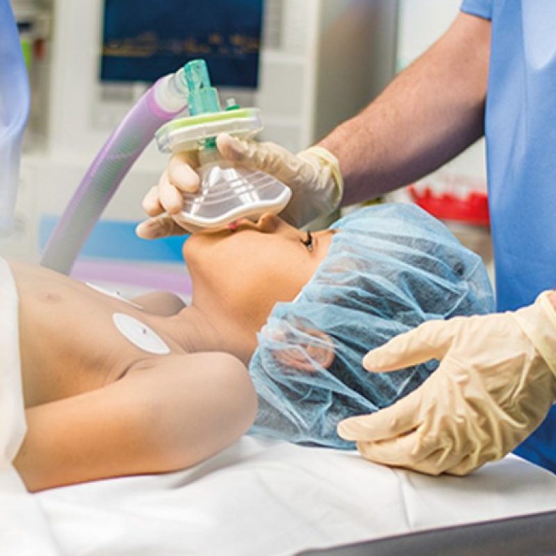 Blurred shot of a child with oxygen mask lying on bed in operating room.